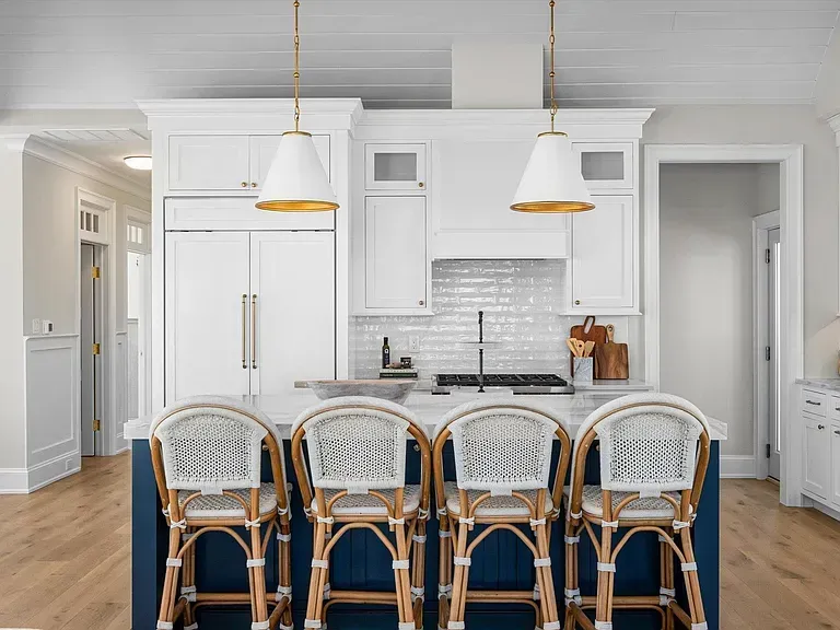 A kitchen with white cabinets and a blue island with wicker chairs.