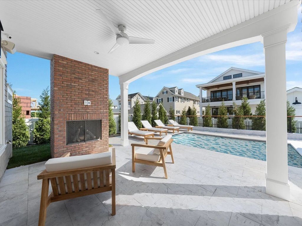 A patio with a fireplace, chairs, and a swimming pool.