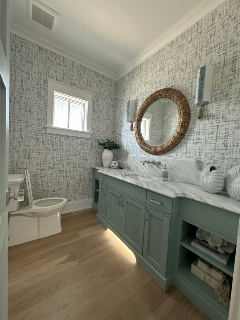 A bathroom with a toilet, sink, mirror, and window.