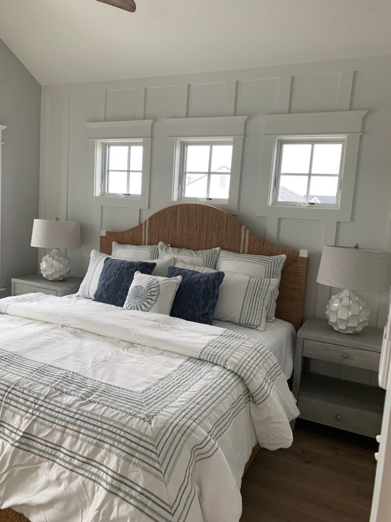 A bedroom with a bed, nightstands, lamps, and windows.