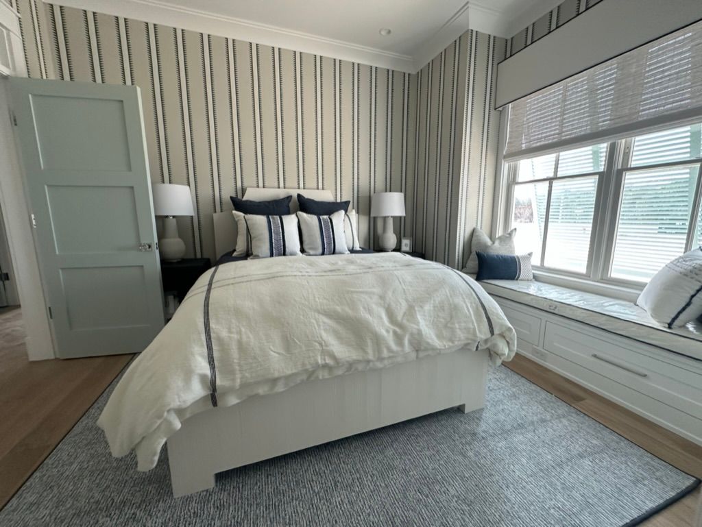 A bedroom with a bed, window seat, and striped wallpaper.