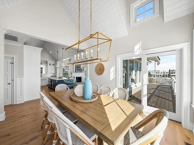 A dining room with a wooden table and chairs and a chandelier hanging from the ceiling.