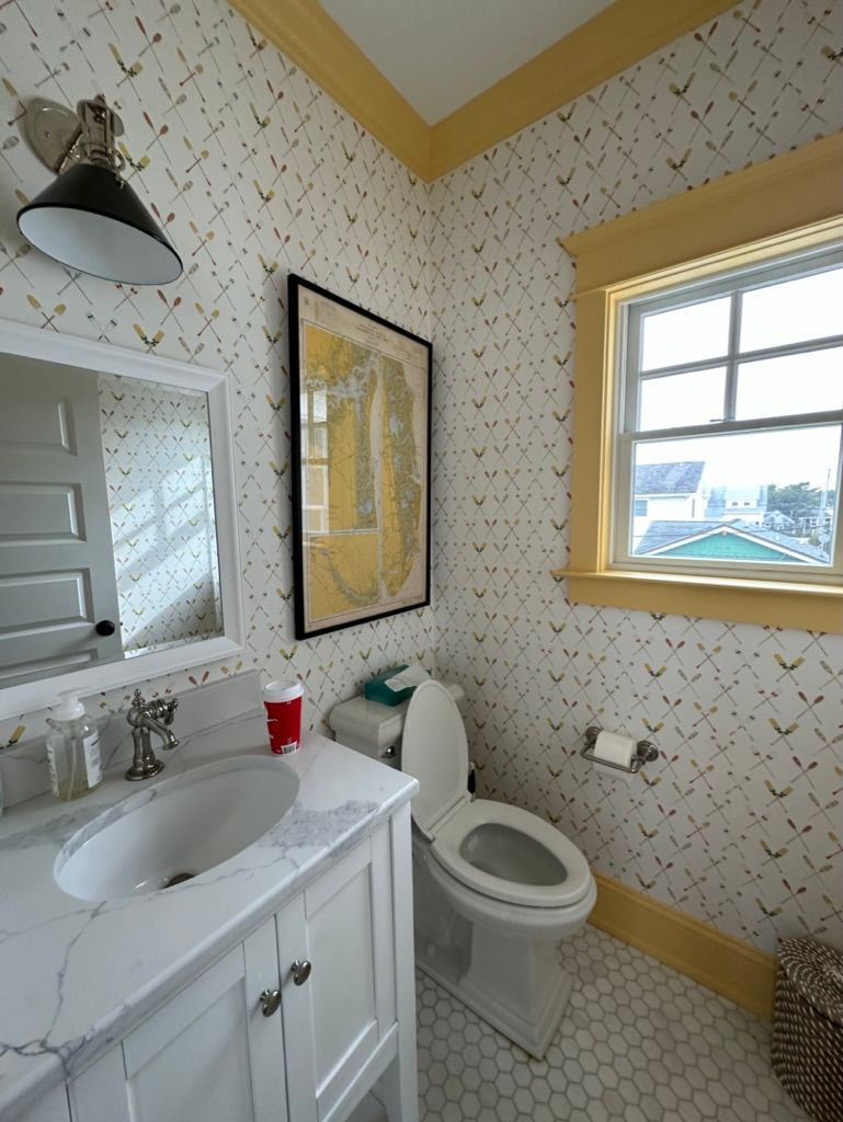 A bathroom with a toilet, sink, mirror, and window
