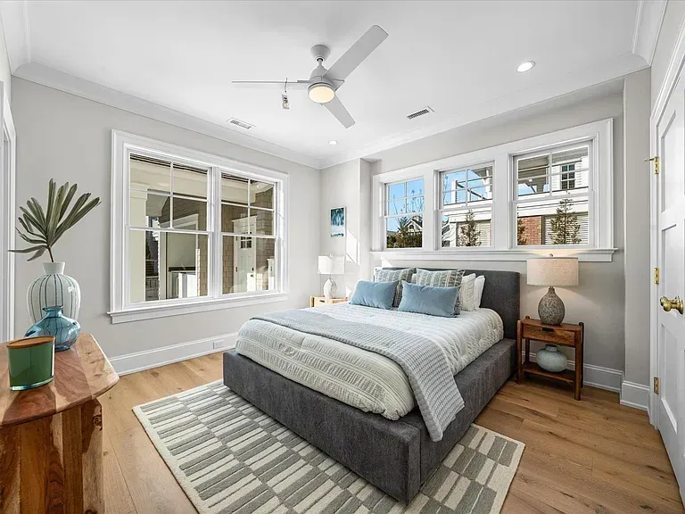 A bedroom with a bed, ceiling fan, windows, and a rug.