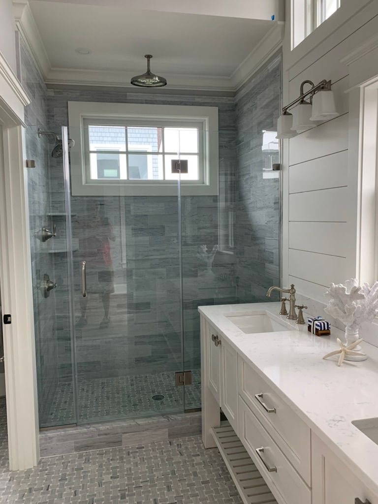 A bathroom with a walk-in shower, sink, mirror, and window.