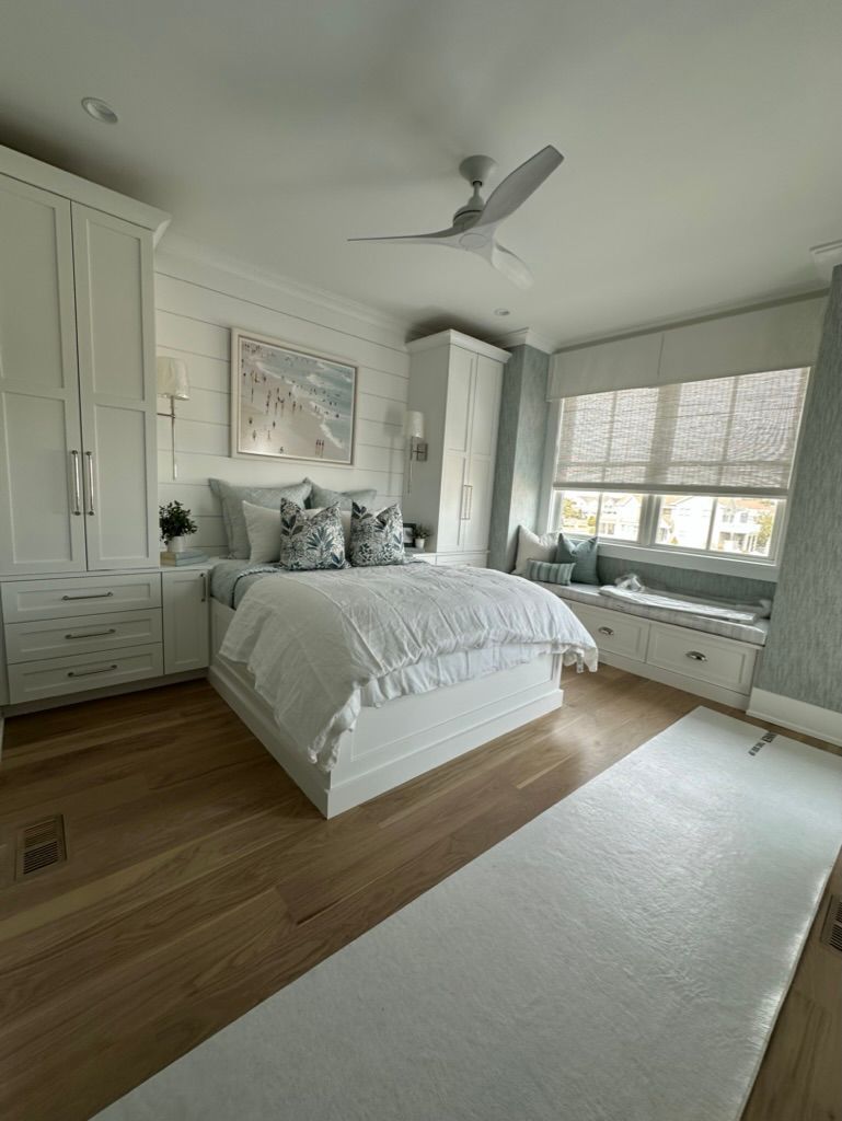 A bedroom with a bed, a window seat, a ceiling fan, and a rug.