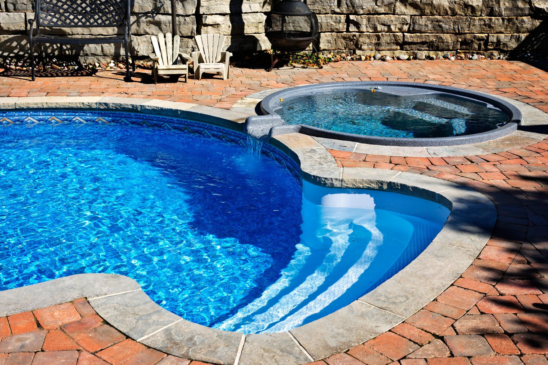 A swimming pool and a hot tub are sitting on a brick patio.