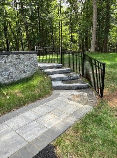 Stone steps with a black metal fence leading up to a forest path and garden.