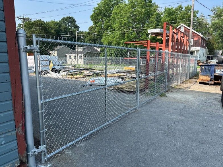 Chain-link fence gate on asphalt; in the background, a construction site with building materials.
