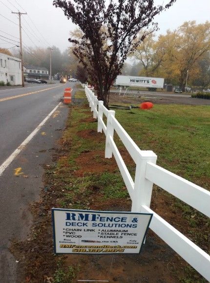 White two-rail fence along a road, sign in front for RM Fence & Deck Solutions. Foggy day.
