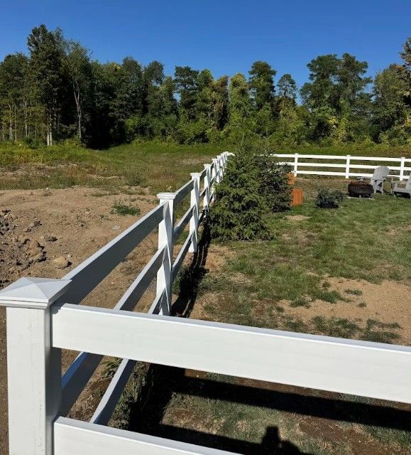 White fence in a grassy yard, trees in the background, blue sky.