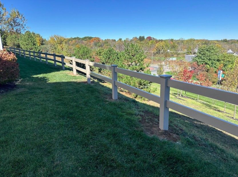 Tan fence on a grassy hill overlooking trees under a clear blue sky.