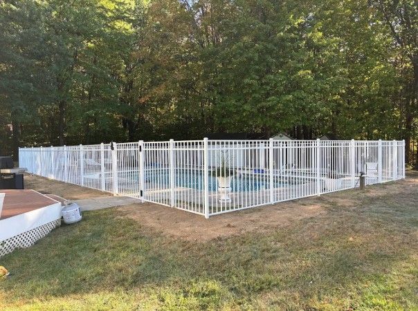White fenced-in pool in a grassy yard, surrounded by trees.
