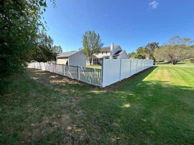 White picket fence surrounding a grassy yard with a house in the background on a sunny day.