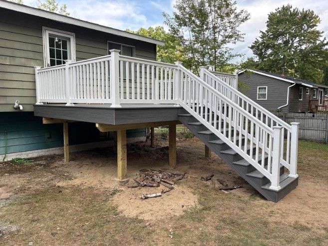 White railing and stairs on a raised deck attached to a house with green siding.