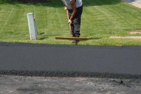 A man is laying asphalt on the side of a road.