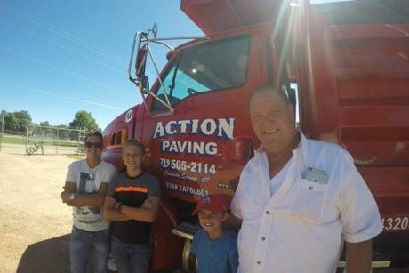 A group of people are standing in front of a red action paving truck.