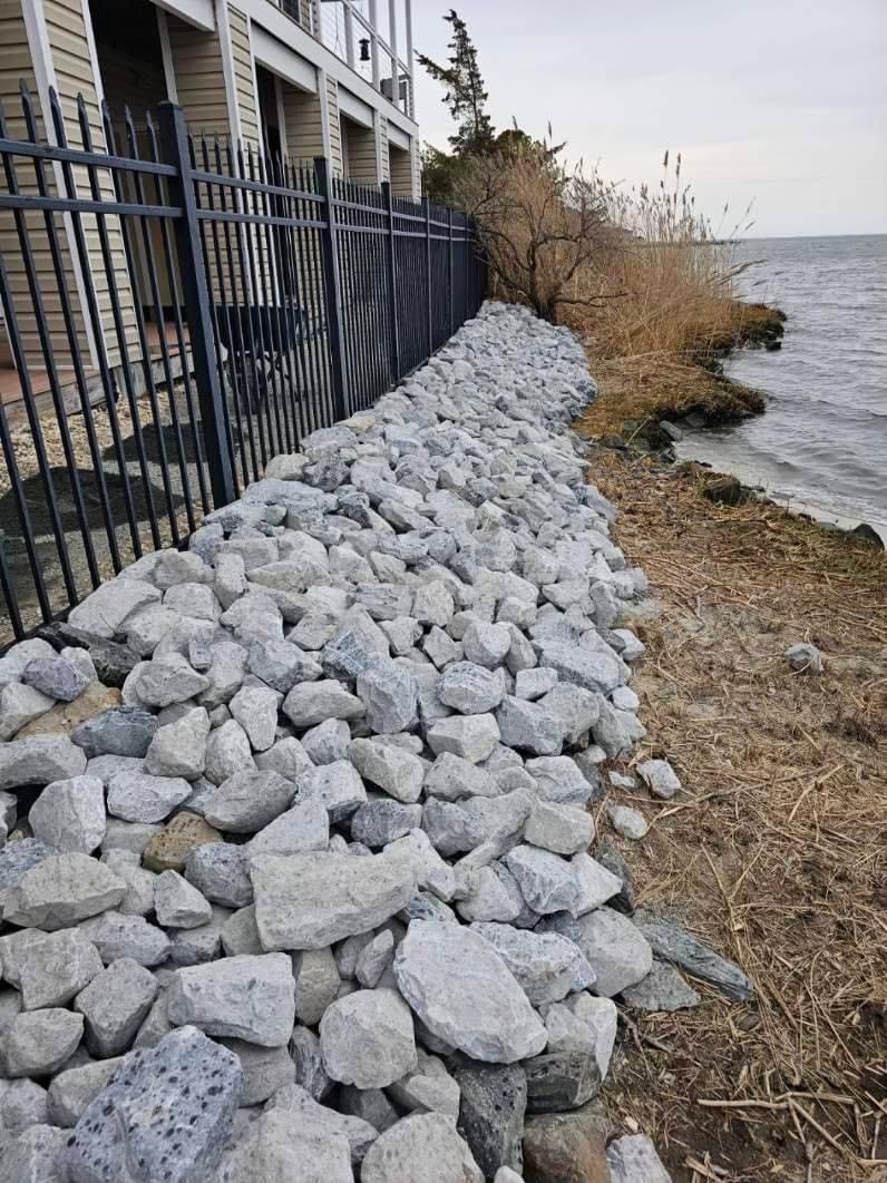 a pile of rocks on the shore of a lake next to a fence .