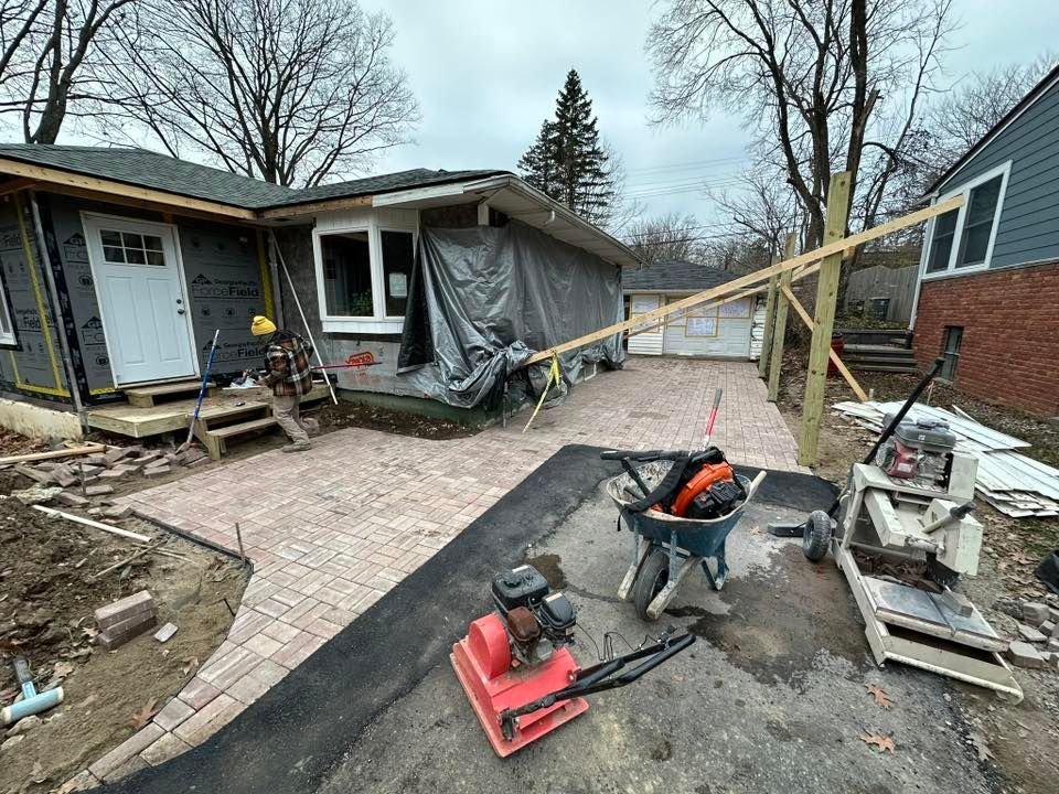 Damaged house with tarp-covered wall, fallen porch, and construction tools in a muddy yard