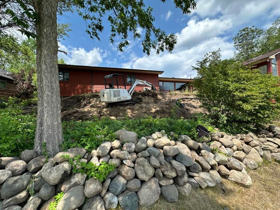 Red house on a rocky hillside with a car parked on the slope and a stone retaining wall in front