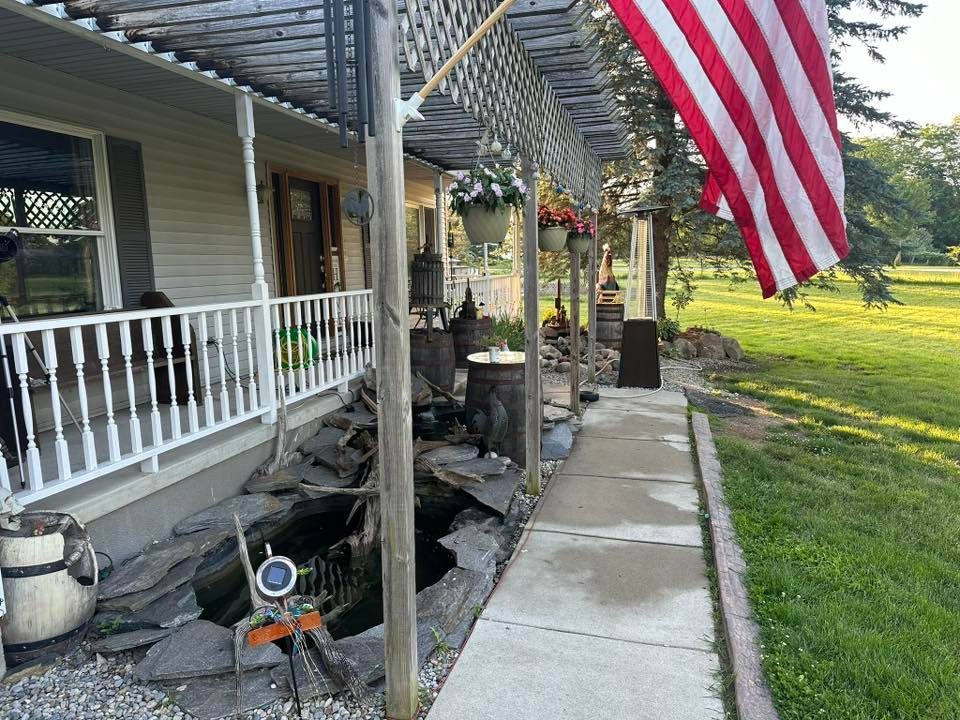 Porch with white railing, hanging American flag, and a concrete walkway beside a grassy yard