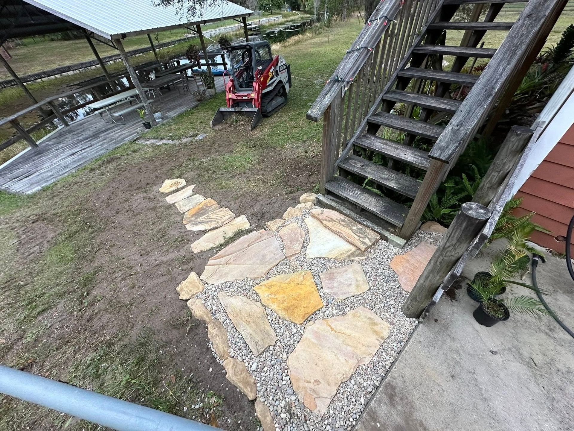 Stone path beside outdoor stairs with a red tractor in a muddy yard
