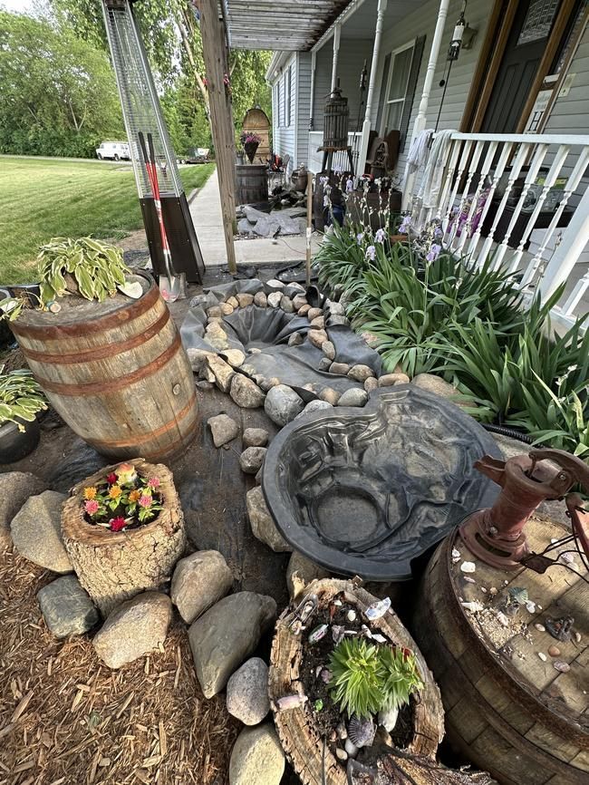 Garden path with rocks, barrel planters, and decorative planters beside a porch