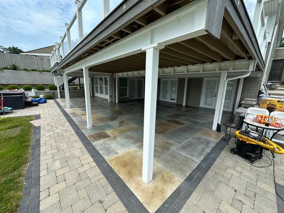 Covered patio under a deck with white posts, gray pavers, and a yellow generator on the right.