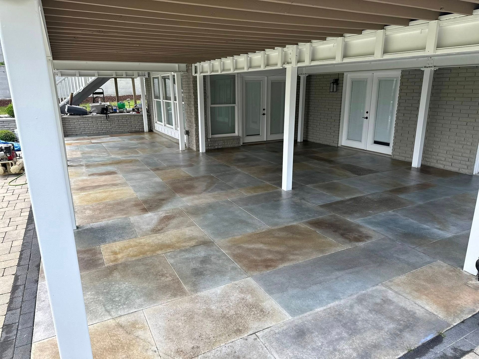 Covered outdoor patio with tiled floor, white columns, and glass doors along a brick building