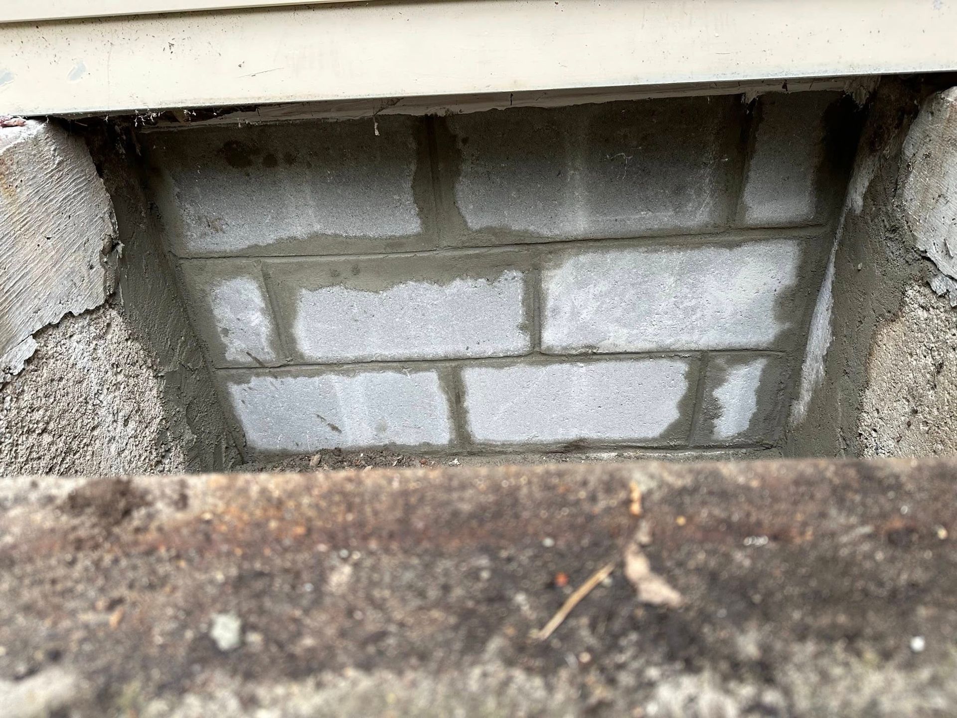 Close-up of a small concrete wall opening with cinder blocks and a rusty ledge.