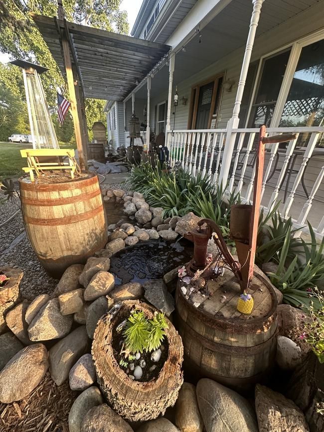 Rustic porch garden with wooden barrels, rocks, and potted succulents beside a house walkway