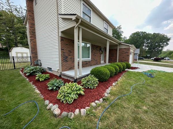 Suburban house with a covered porch, red mulch flower bed, and trimmed shrubs along the foundation