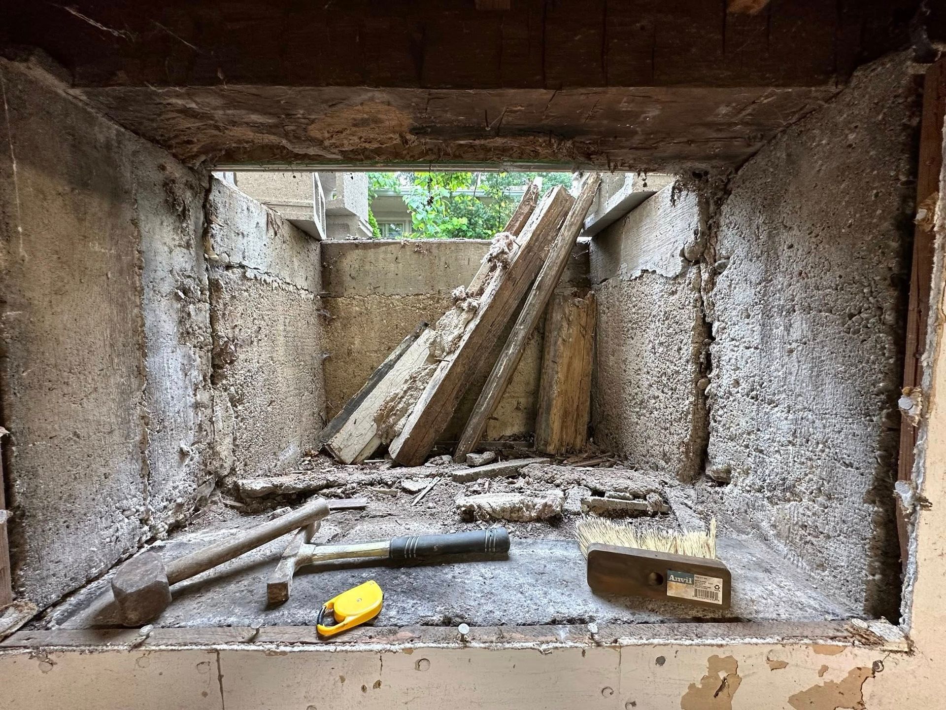 Crumbling concrete tunnel with wooden supports and debris on the floor, seen from inside toward a small opening.