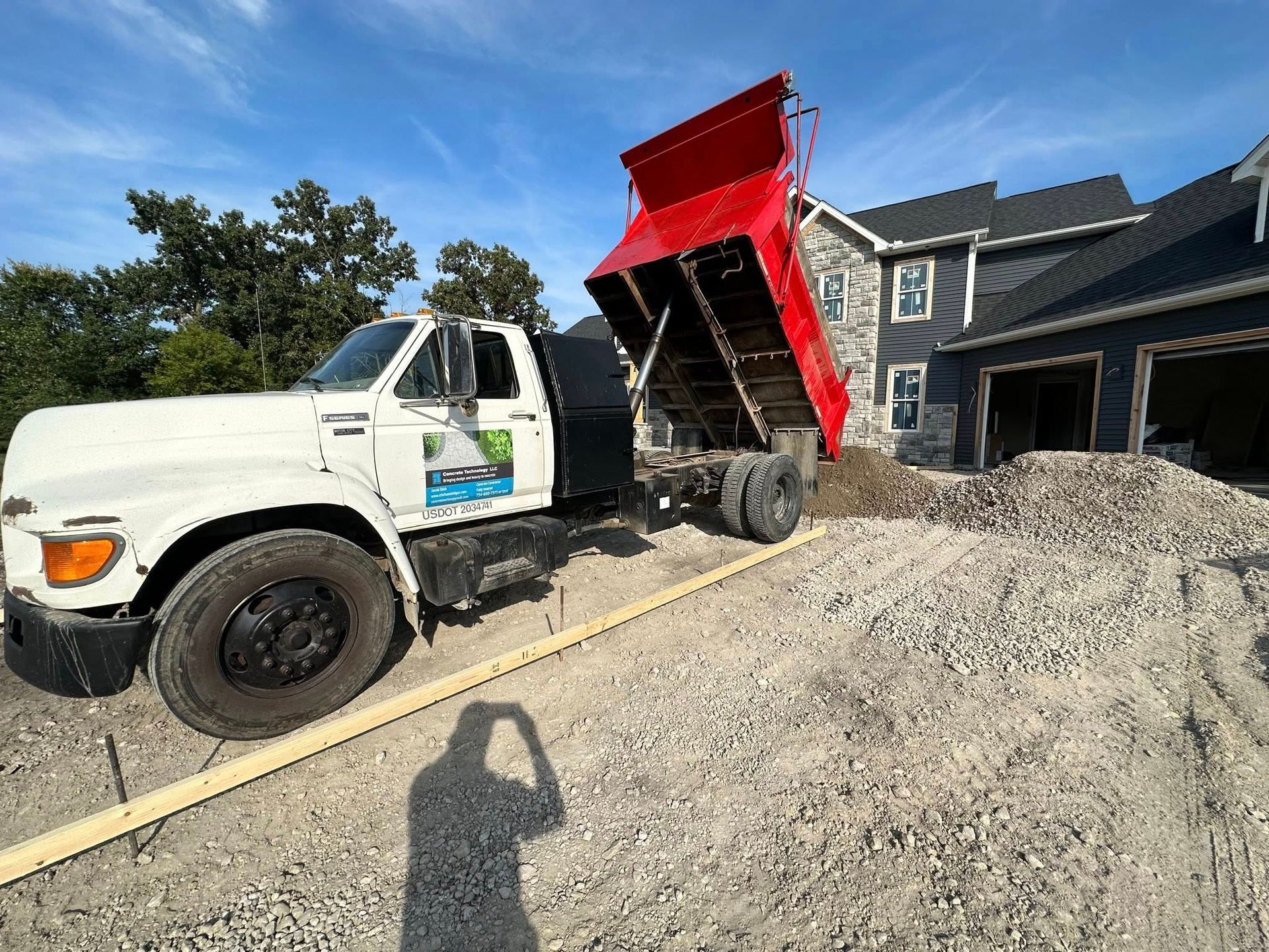 White dump truck unloading gravel at a house construction site under a clear sky
