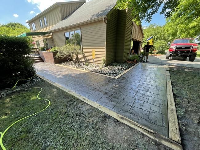 Curved stone walkway beside a beige house, with a red truck parked on the driveway.