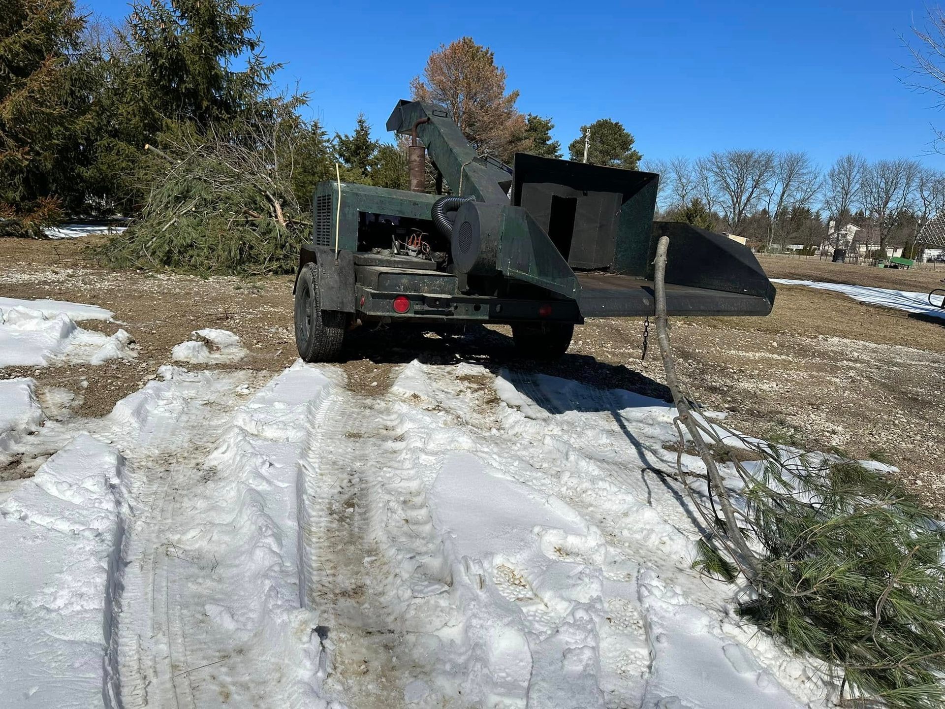 Black truck with large dump bed in a snowy, muddy lot under a clear blue sky.