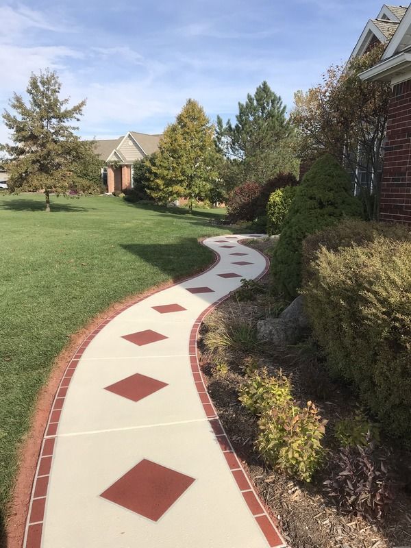 Curved white garden walkway with red diamond accents beside a brick house and green lawn