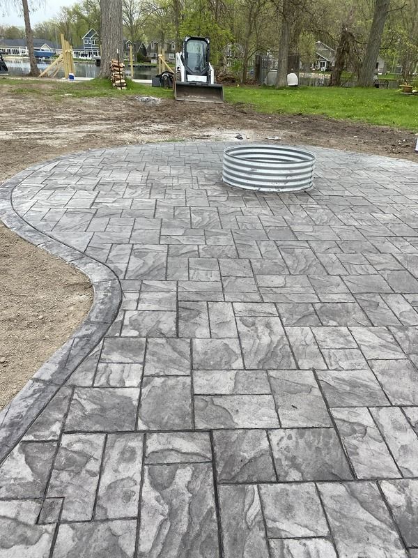 New gray paver patio with a circular metal fire pit in a grassy outdoor area