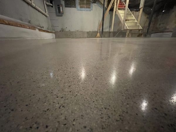 Shiny speckled concrete floor in an industrial space, with reflections of overhead lights and stairs.