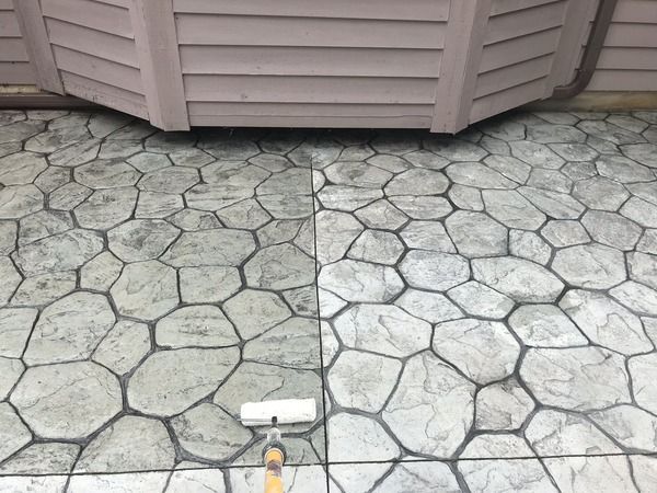 Stone patio with a visible seam between old weathered slabs and newer lighter pavers beside a house wall.