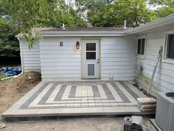 Patio deck with striped paver pattern leading to a back door on a white house
