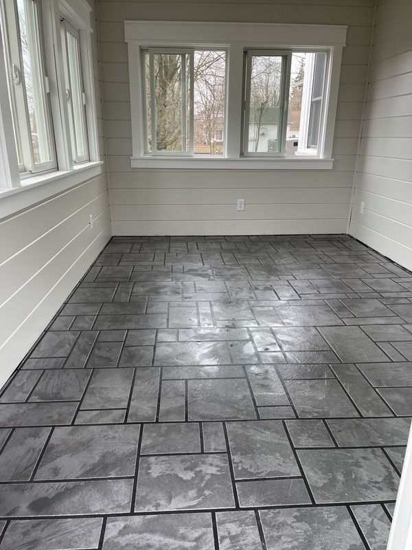 Empty enclosed porch with gray tiled floor and windows on three walls.