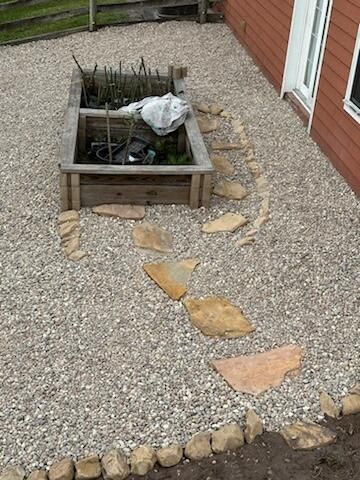 Small gravel garden with a raised square planter, stone stepping path, and a covered fountain beside a brick house