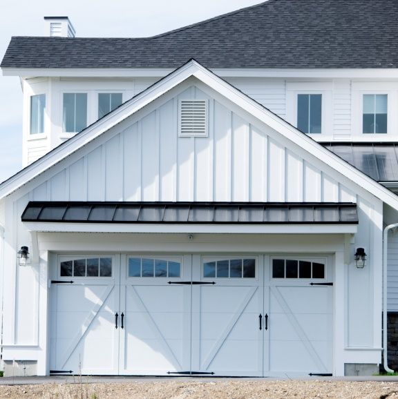 A white house with a black roof and white garage doors