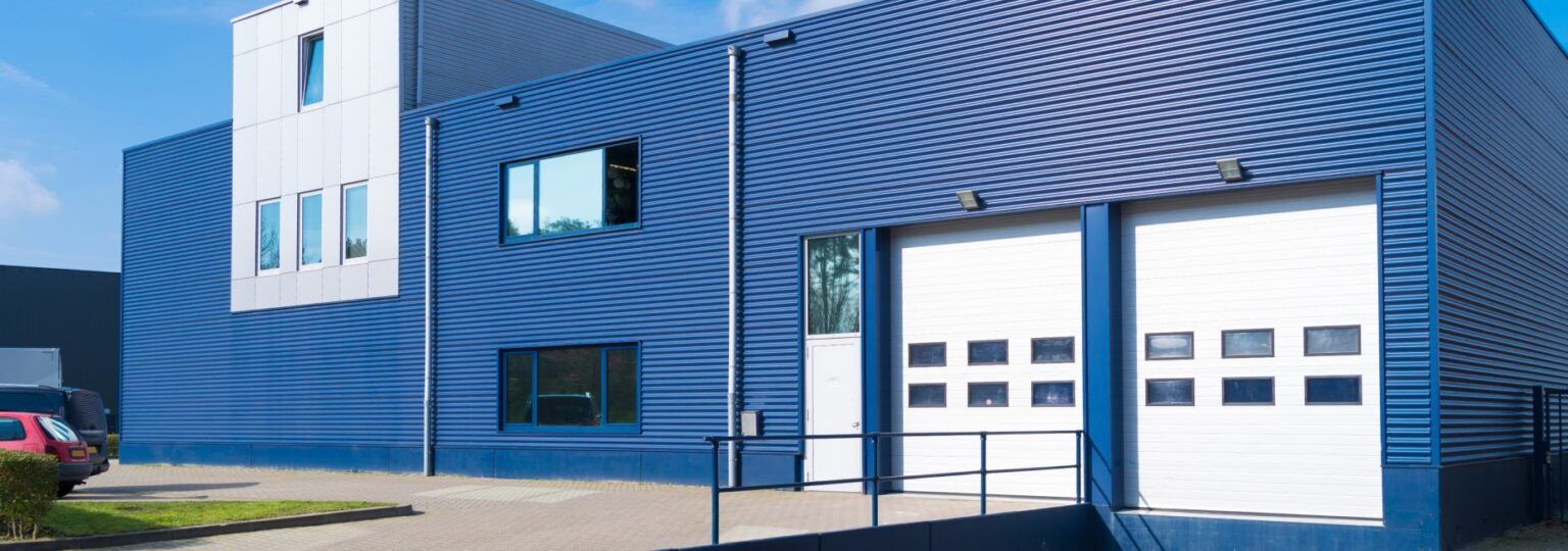 A large blue building with white garage doors and a car parked in front of it.