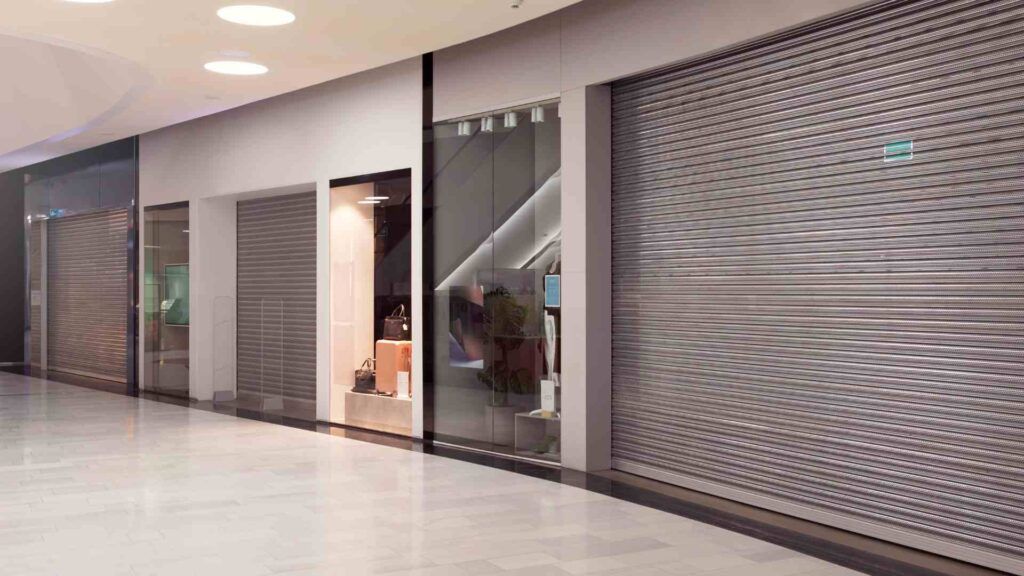 A row of store fronts in a shopping mall with roller shutters.