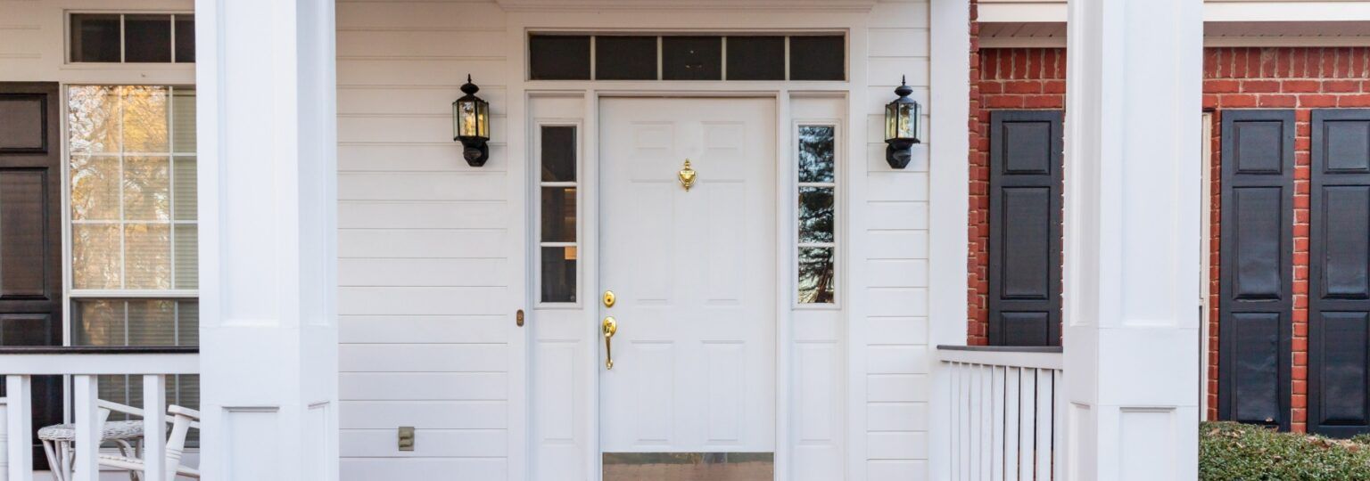 The front door of a white house with black shutters and a porch.