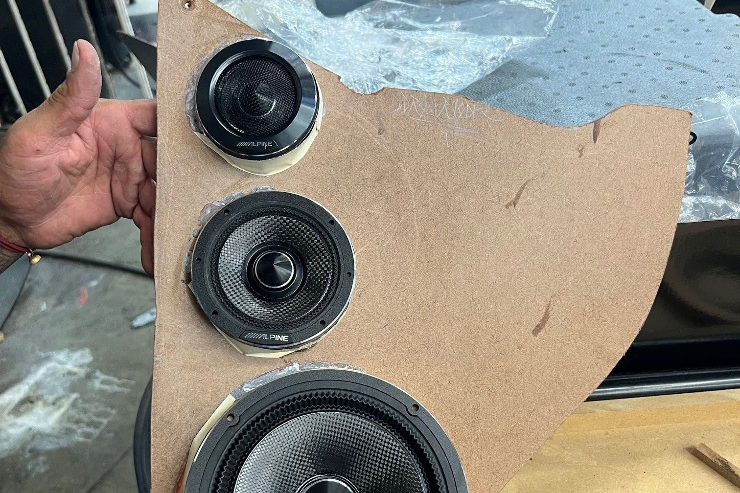 A person is holding a piece of wood with three speakers on it.