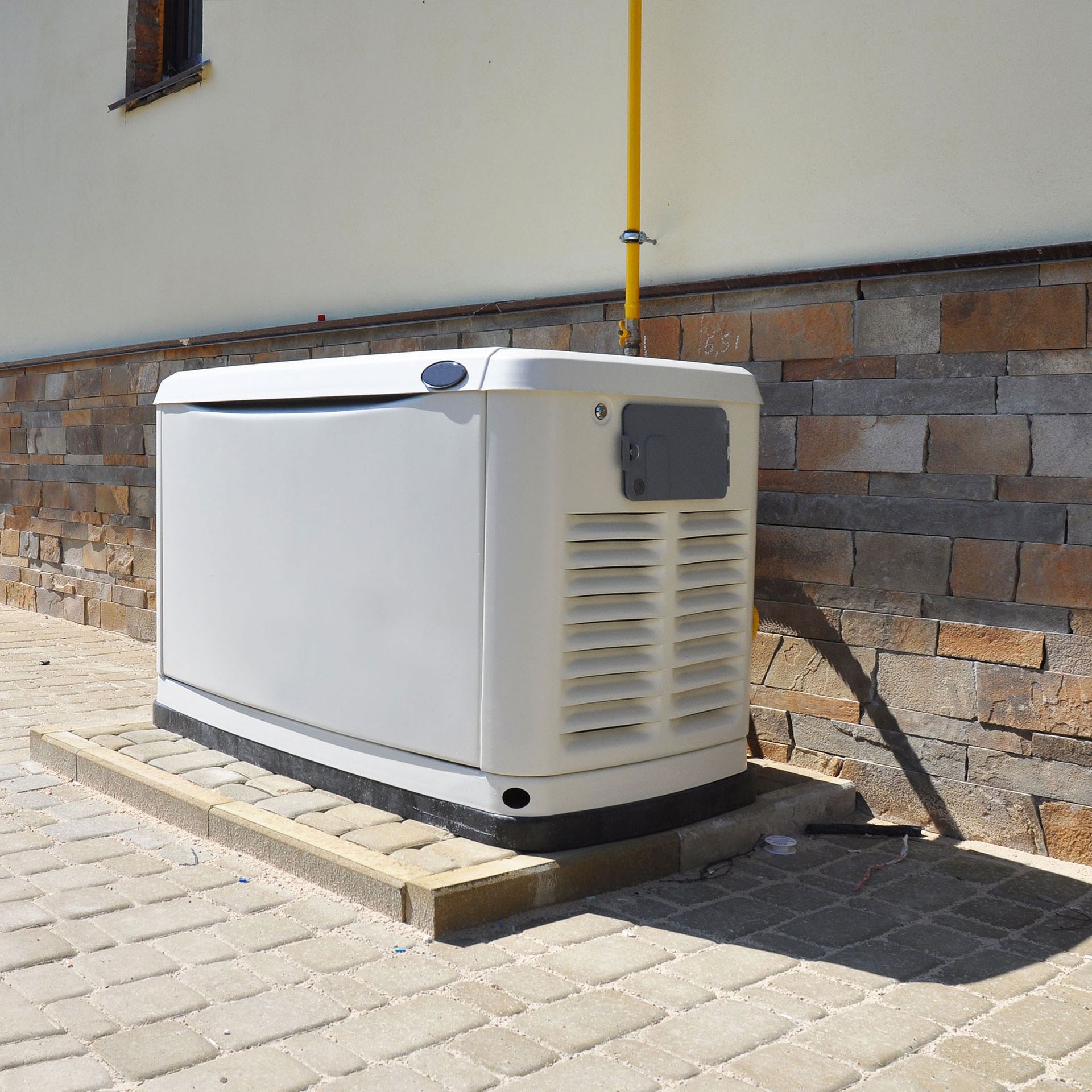 A white generator is sitting on a sidewalk next to a brick wall.