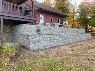 A large stone wall is being built in front of a red house